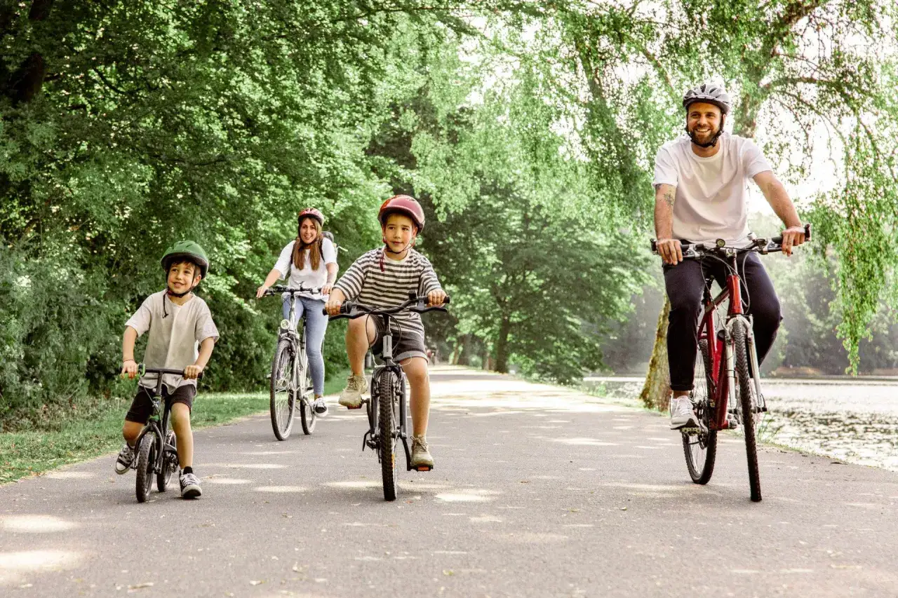Familie genie&szlig;t eine Fahrradtour mit Kindern in NRW. Vater, Mutter und zwei Jungen radeln auf einem asphaltierten Weg durch eine gr&uuml;ne Allee.