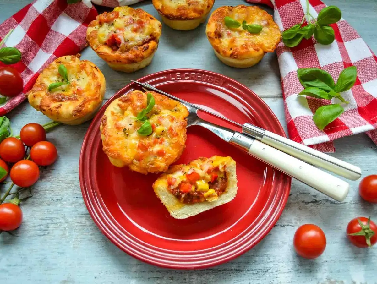 Leckere Pizza Muffins mit geschmolzenem K&auml;se und frischem Basilikum, garniert mit Kirschtomaten.