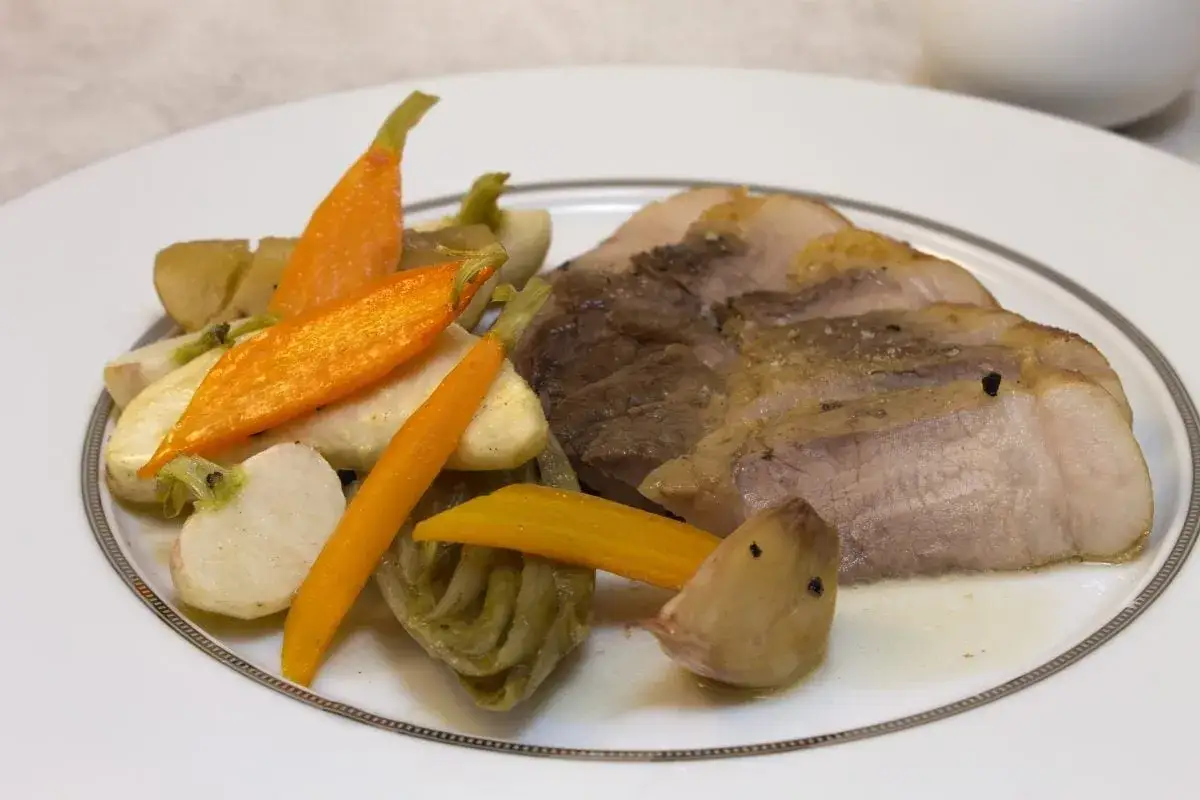 Tranches de rouelle de porc rôti avec carottes et navets glacés, un plat savoureux.
