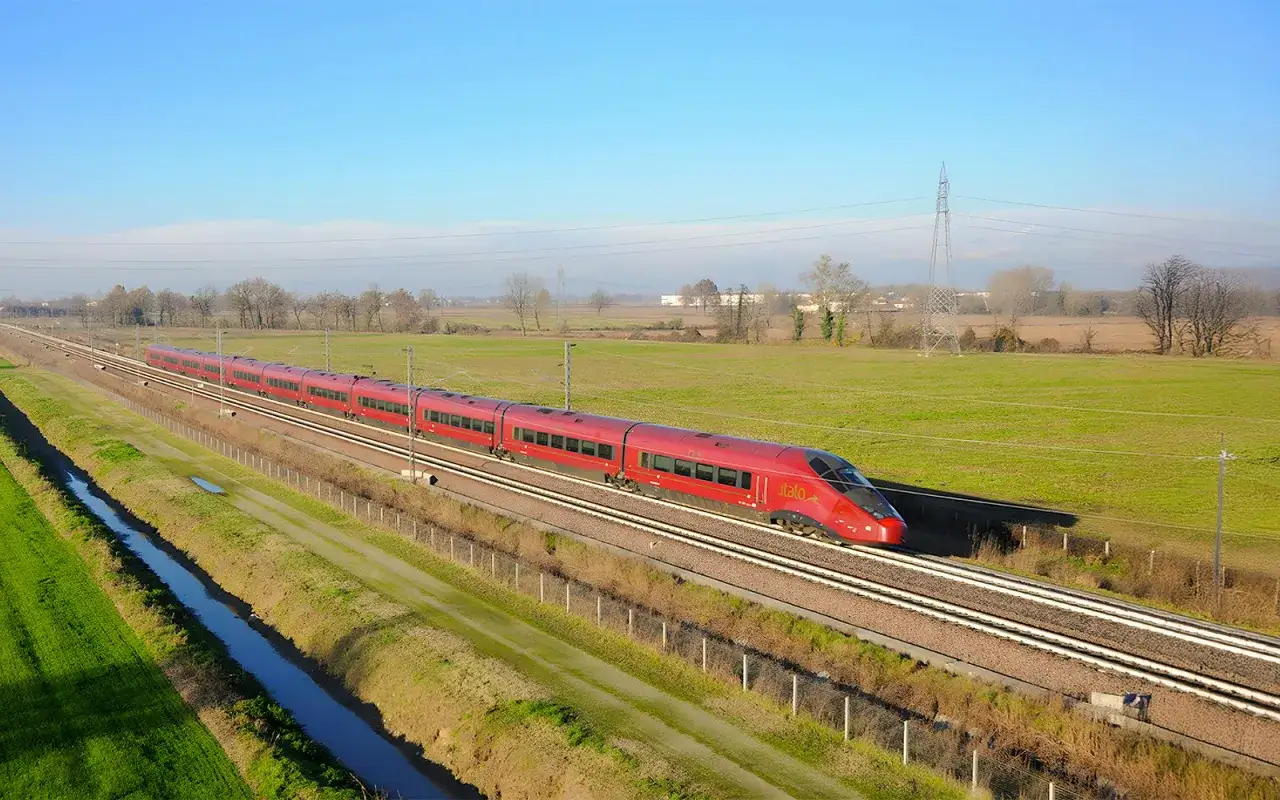 Le train rouge Italo file sur les rails, reliant Rome à Naples à travers la campagne italienne verdoyante.