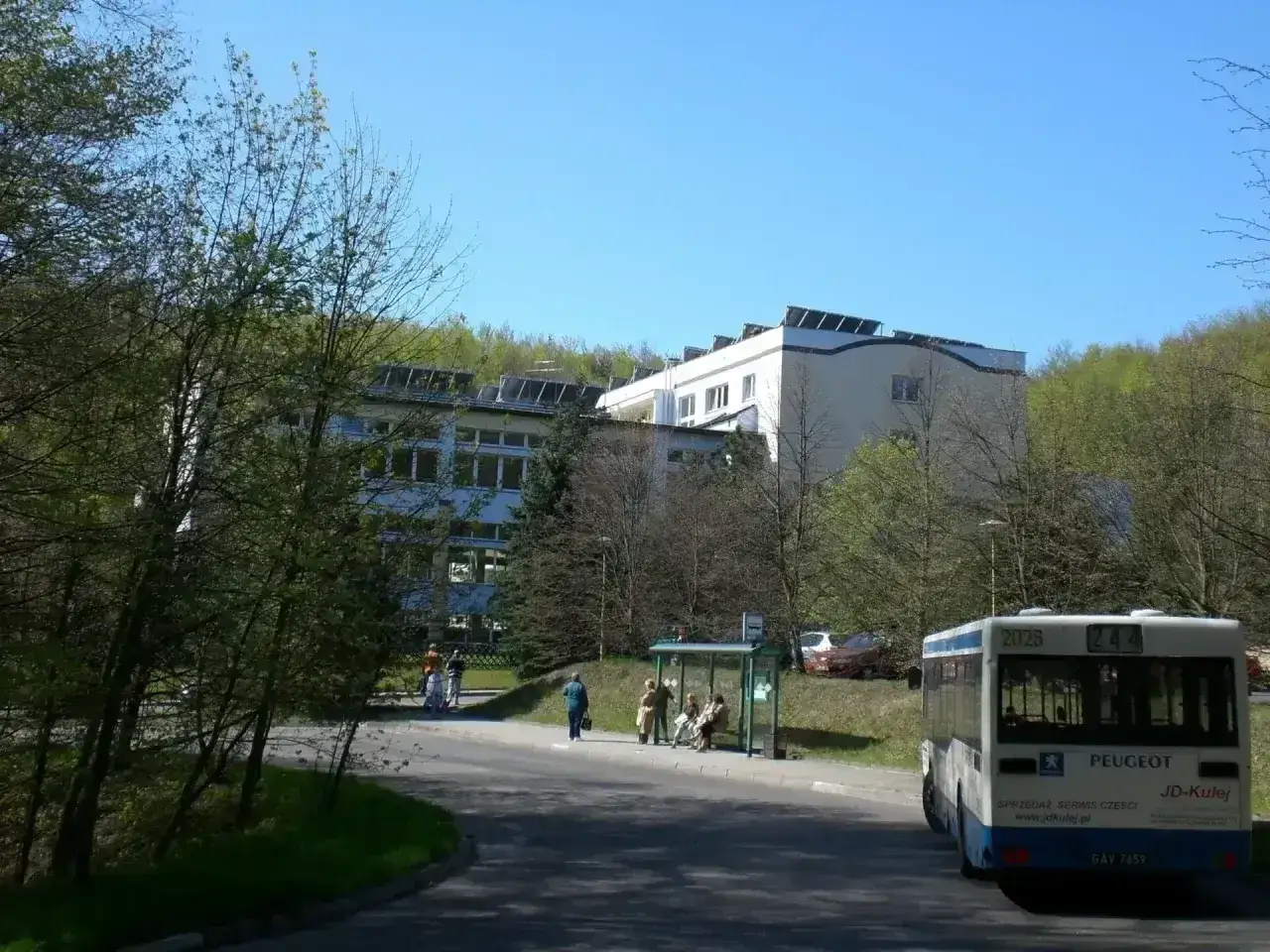 Sanatorium uzdrowiskowe „Leśnik” z panelami słonecznymi na dachu, z autobusem na przystanku.