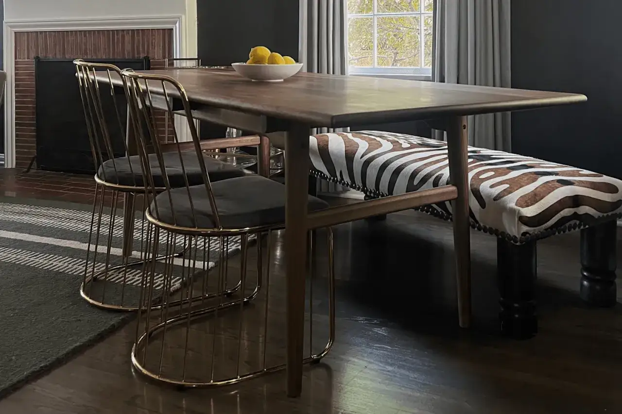 A dining set with mid century modern wood colors, featuring a dark wood table, gold wire chairs, and a zebra-print bench.
