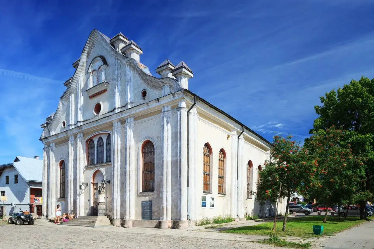 Dawna synagoga, biała, z charakterystycznym dachem i oknami, stoi pod błękitnym niebem. Szalom!