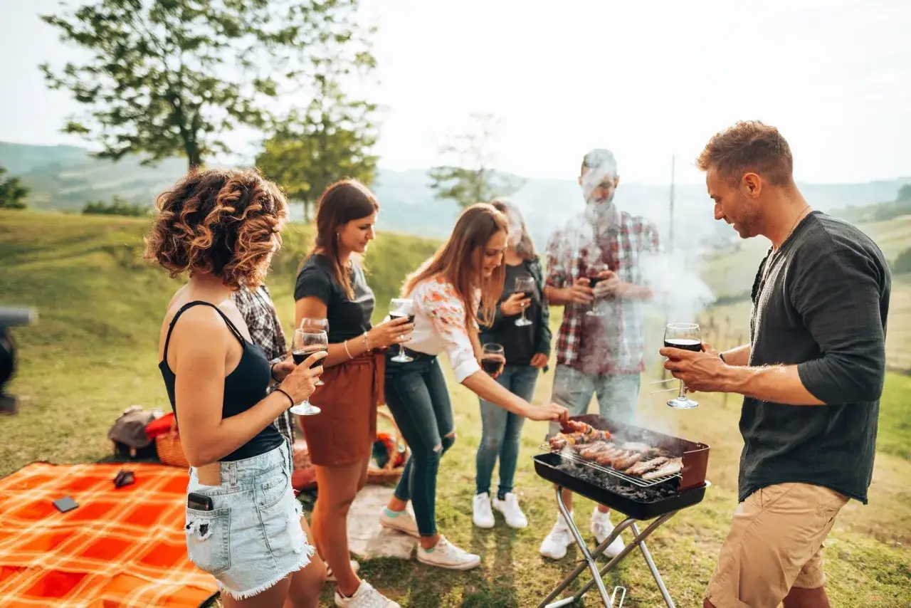 Un groupe d'amis profite d'un barbecue convivial en plein air, savourant des brochettes et du vin rouge dans un cadre champ&ecirc;tre.