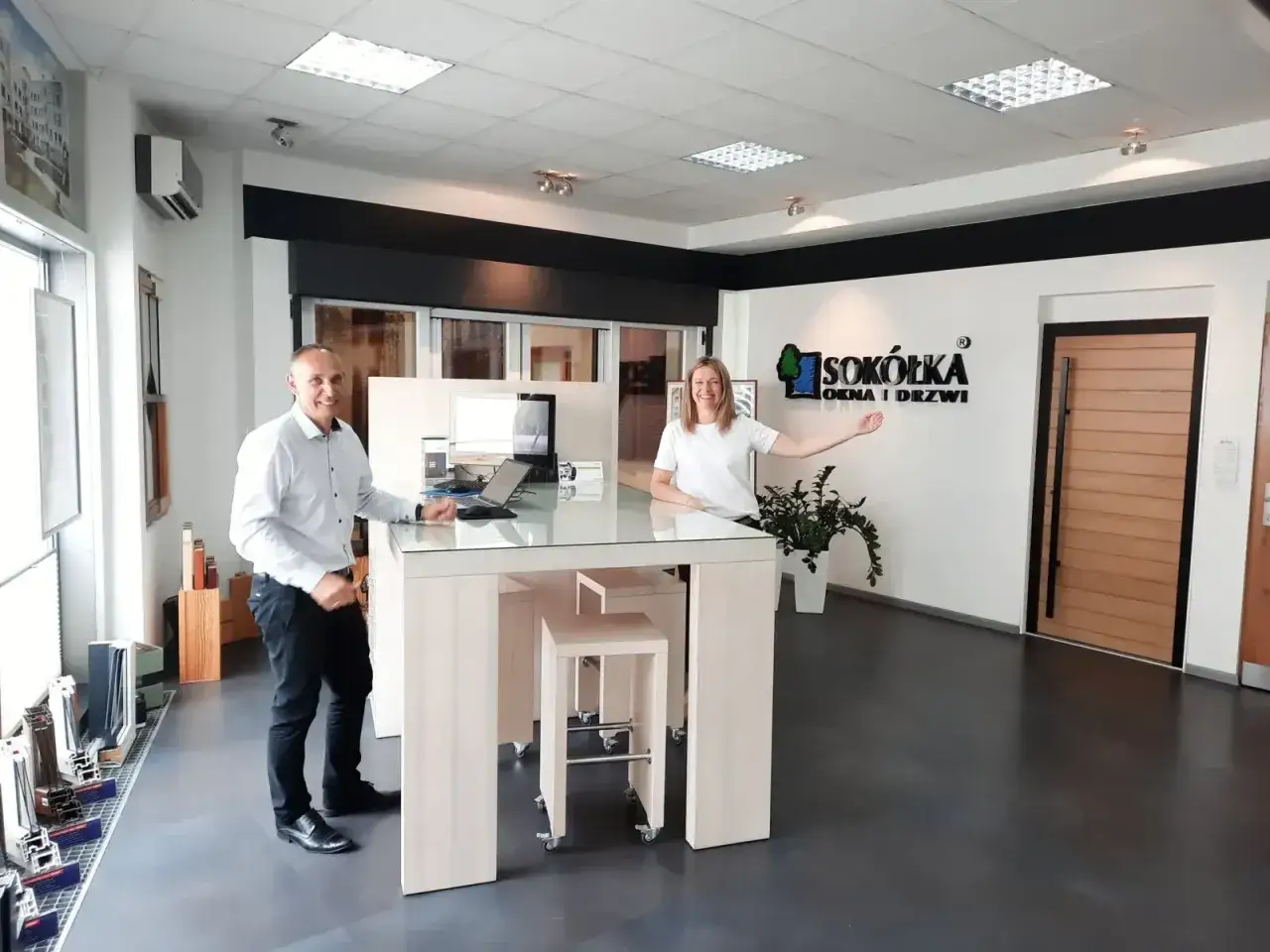 Uśmiechnięci pracownicy w salonie okien i drzwi, z logo firmy 