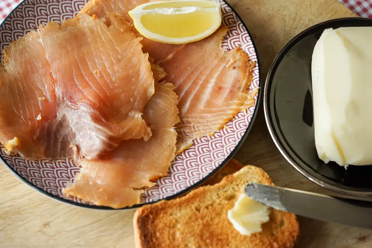 Tranches de saumon fumé sur une assiette décorée, accompagnées d'un quartier de citron, d'une motte de beurre et d'une tartine beurrée.