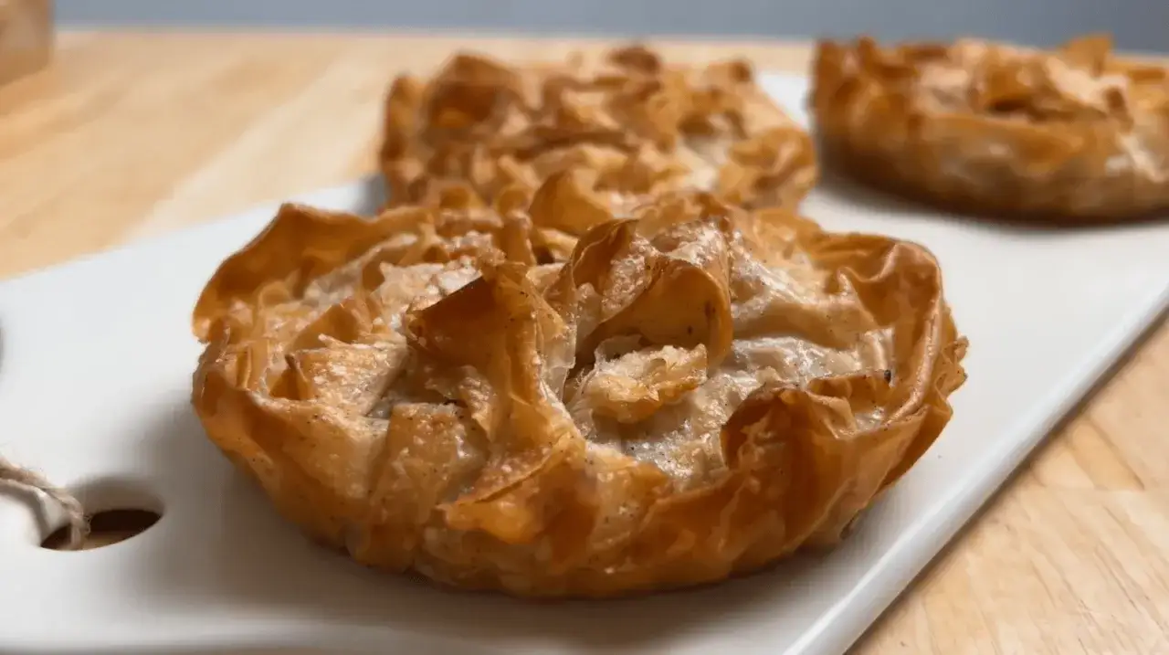 Trois délicieux clafoutis aux pommes individuels, dorés et croustillants, sur une assiette blanche.