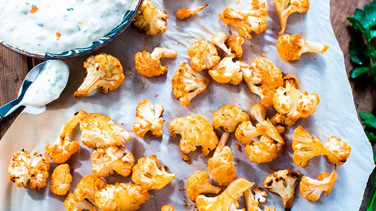 Coliflor asada dorada y crujiente, lista para disfrutar con un dip cremoso.