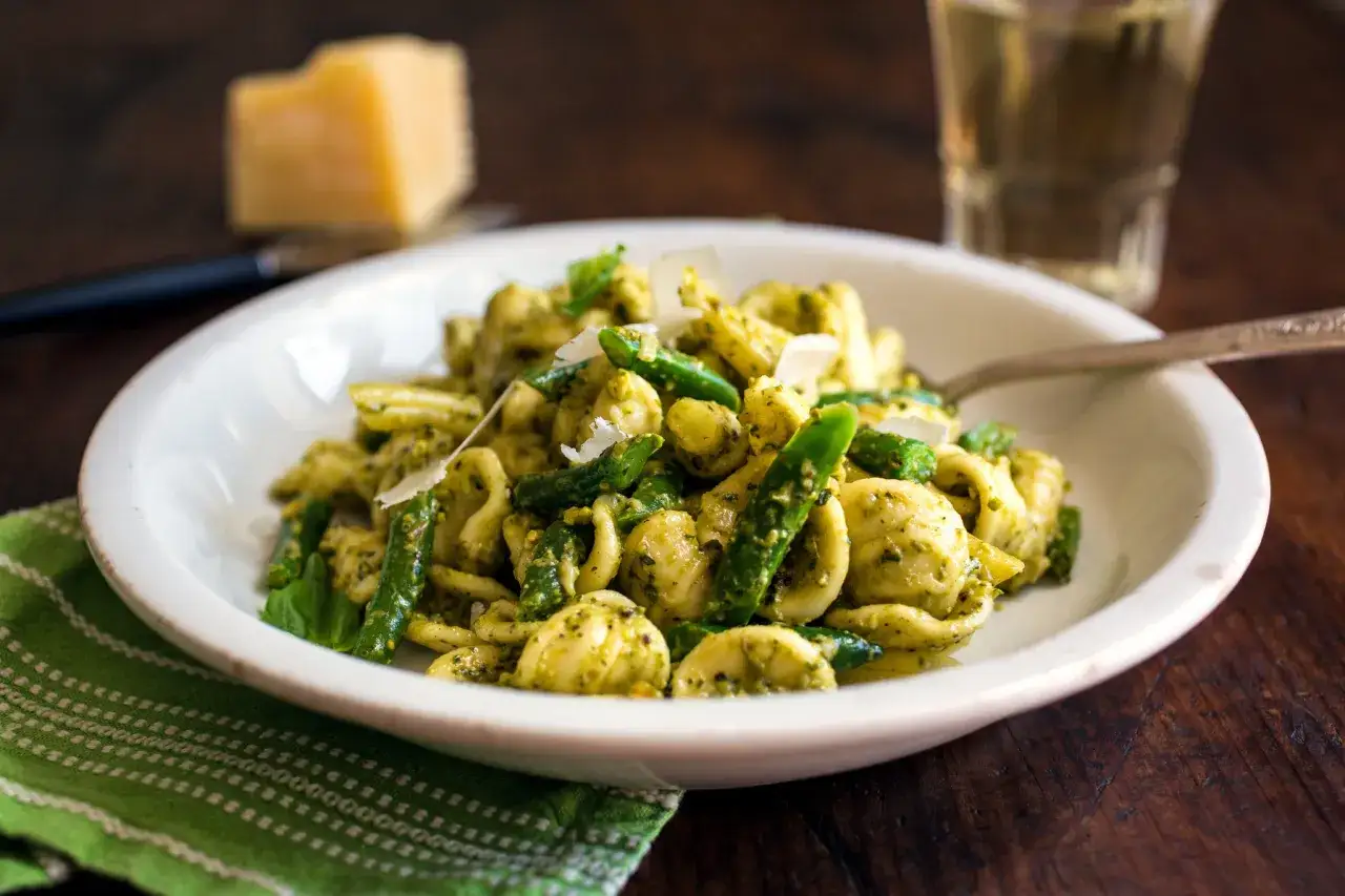 Makaron orecchiette z zielonymi warzywami i kremowym pesto pistacjowym, posypany parmezanem.