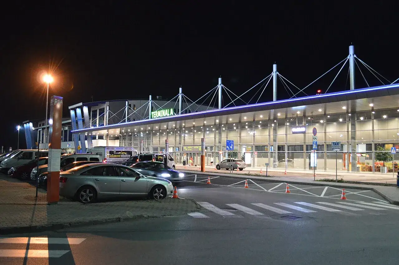 Nocne lotnisko, Terminal A, z samochodami i autokarami. Może to być lotnisko w Warszawie lub Katowicach, gotowe na podróżnych.