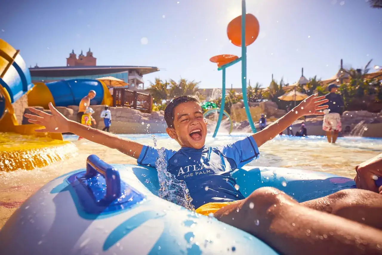 Junge jubelt im Dubai Wasserpark, während er in einem Reifen durch spritzendes Wasser gleitet.