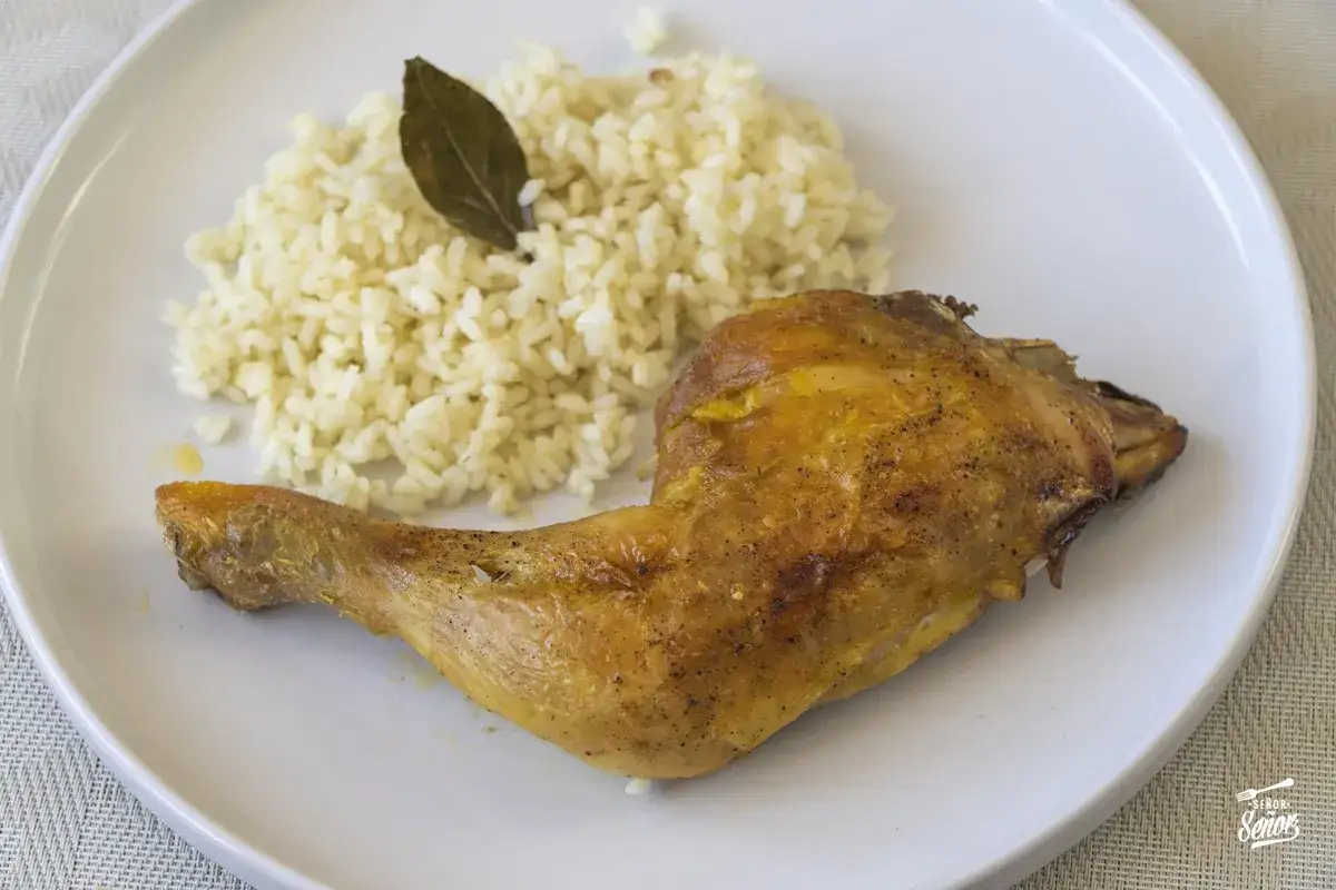 Un contramuslo de pollo dorado y jugoso, acompa&ntilde;ado de arroz blanco y una hoja de laurel.