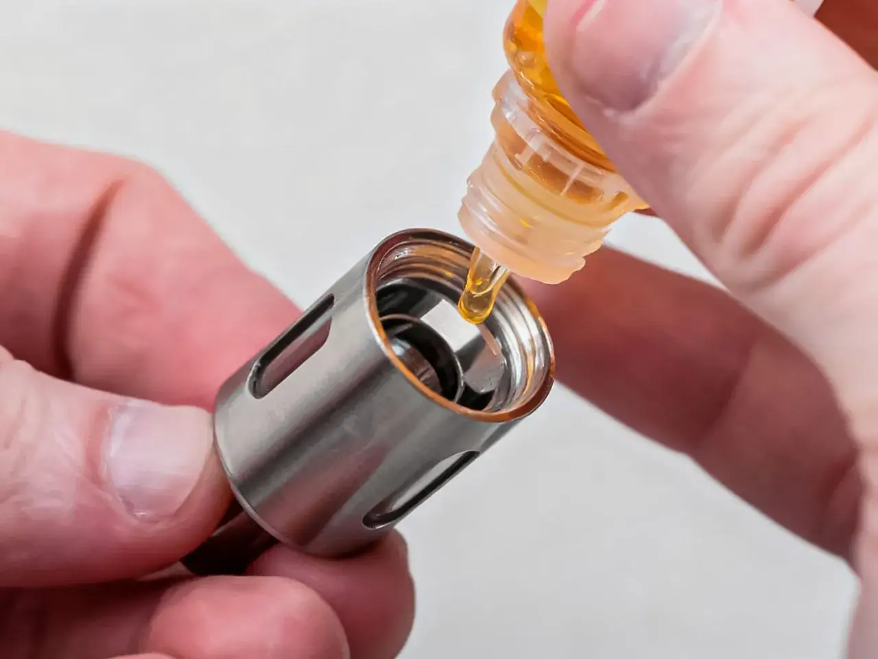 Manos rellenando un atomizador de vapeador con l&iacute;quido. Preparando para cambiar la resistencia Vaporesso.