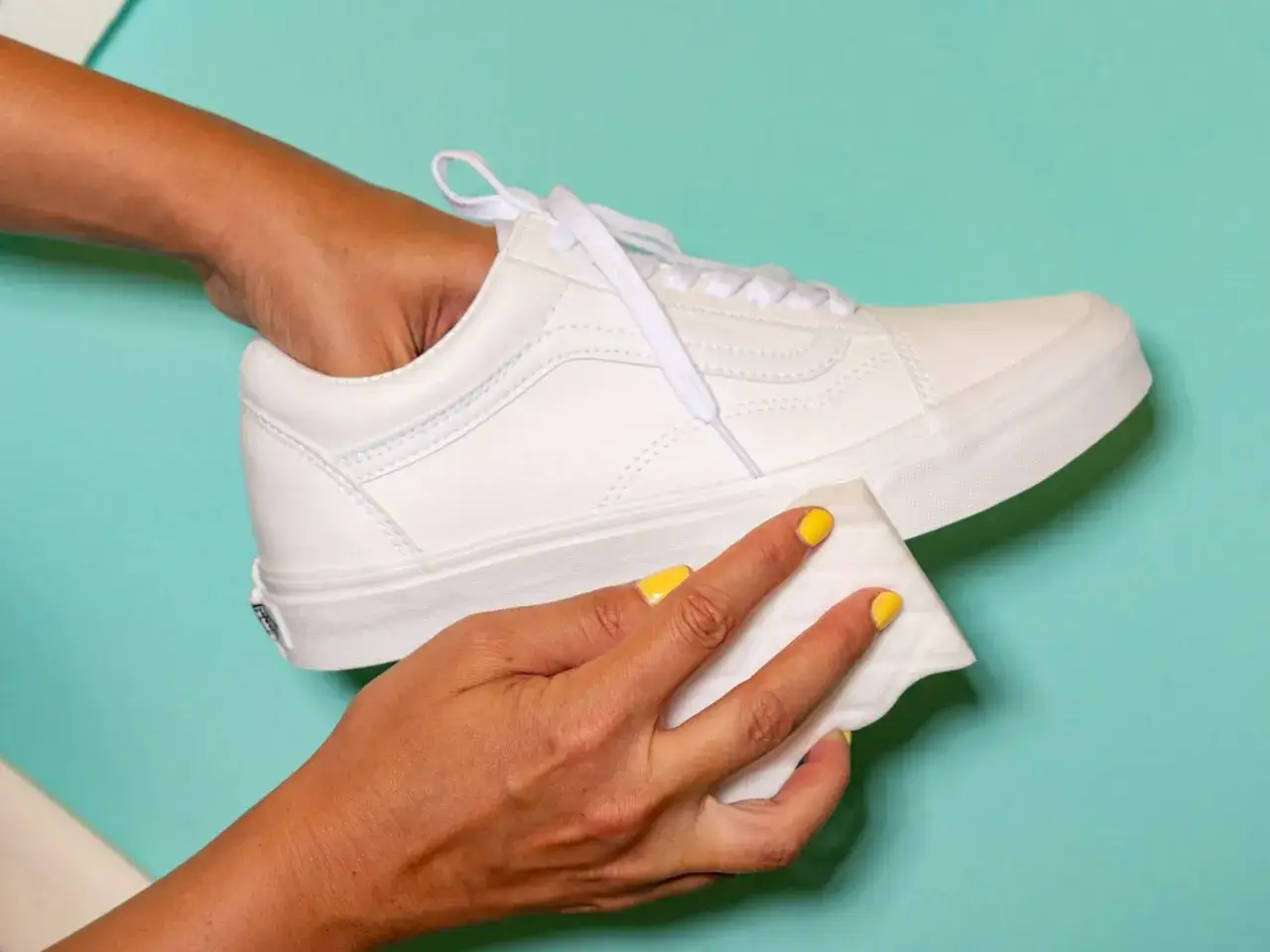 Manos limpiando zapatillas blancas de tela con una toallita.
