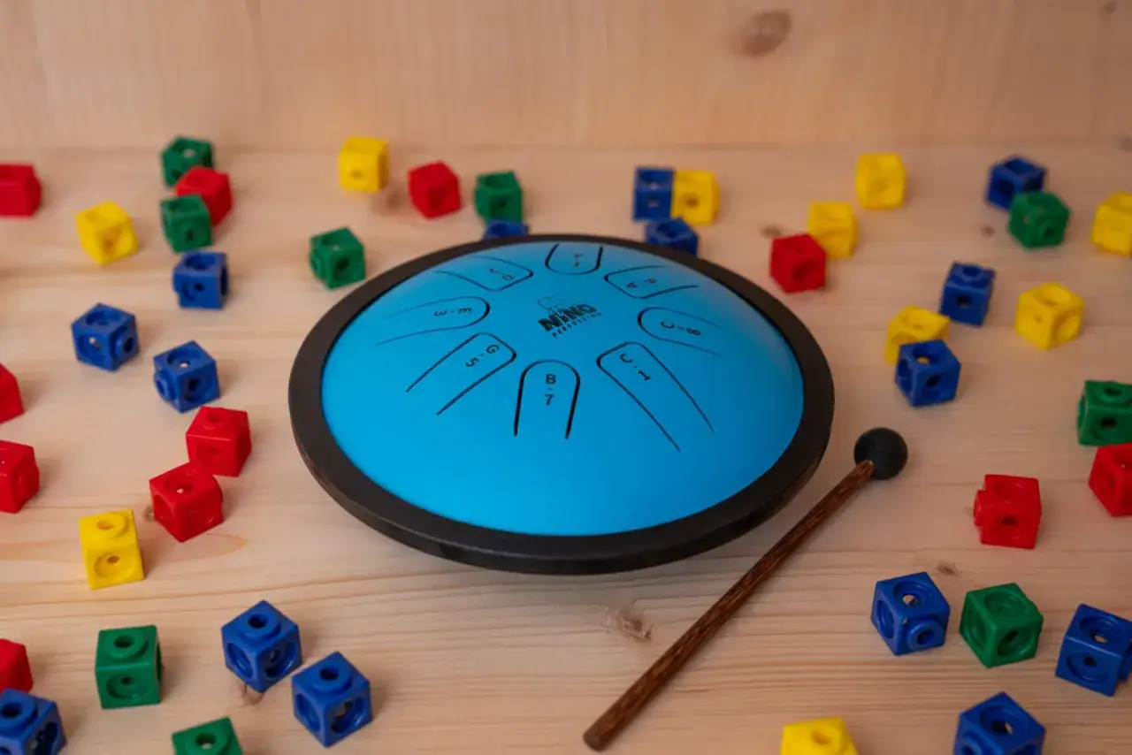 Niebieski steel tongue drum otoczony kolorowymi klockami, gotowy do stworzenia magicznej melodii.