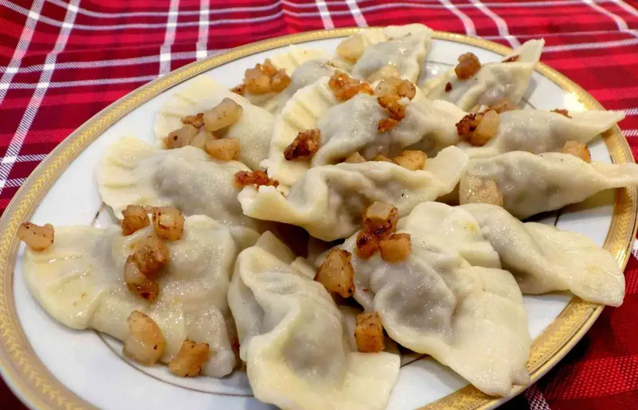 Talerz pełen pysznych, domowych pierogów z białą kiełbasą, posypanych skwarkami.