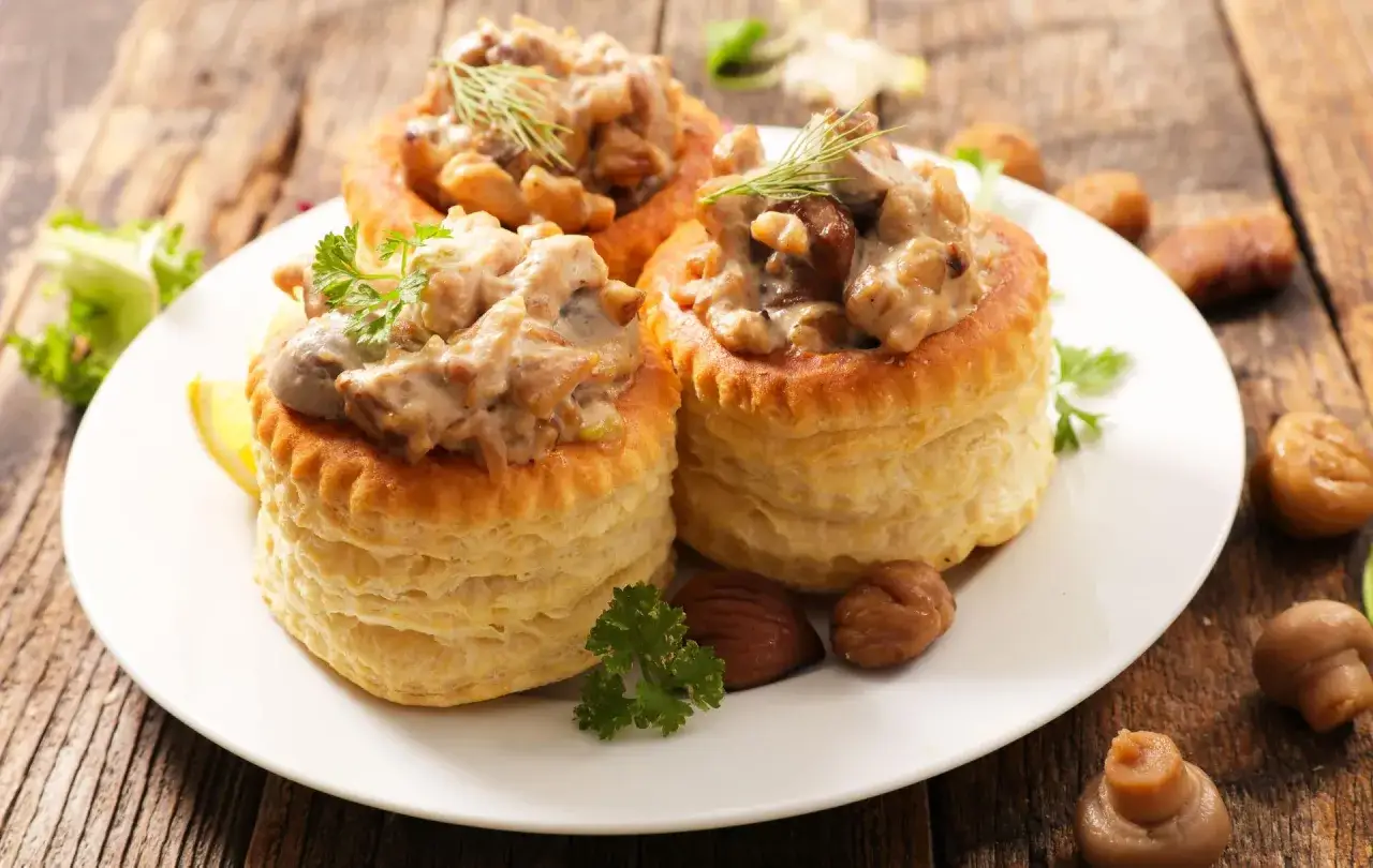 Trois bouchées à la reine poulet garnies d'une sauce crémeuse aux champignons, sur une assiette blanche, avec des marrons et des champignons en garniture.