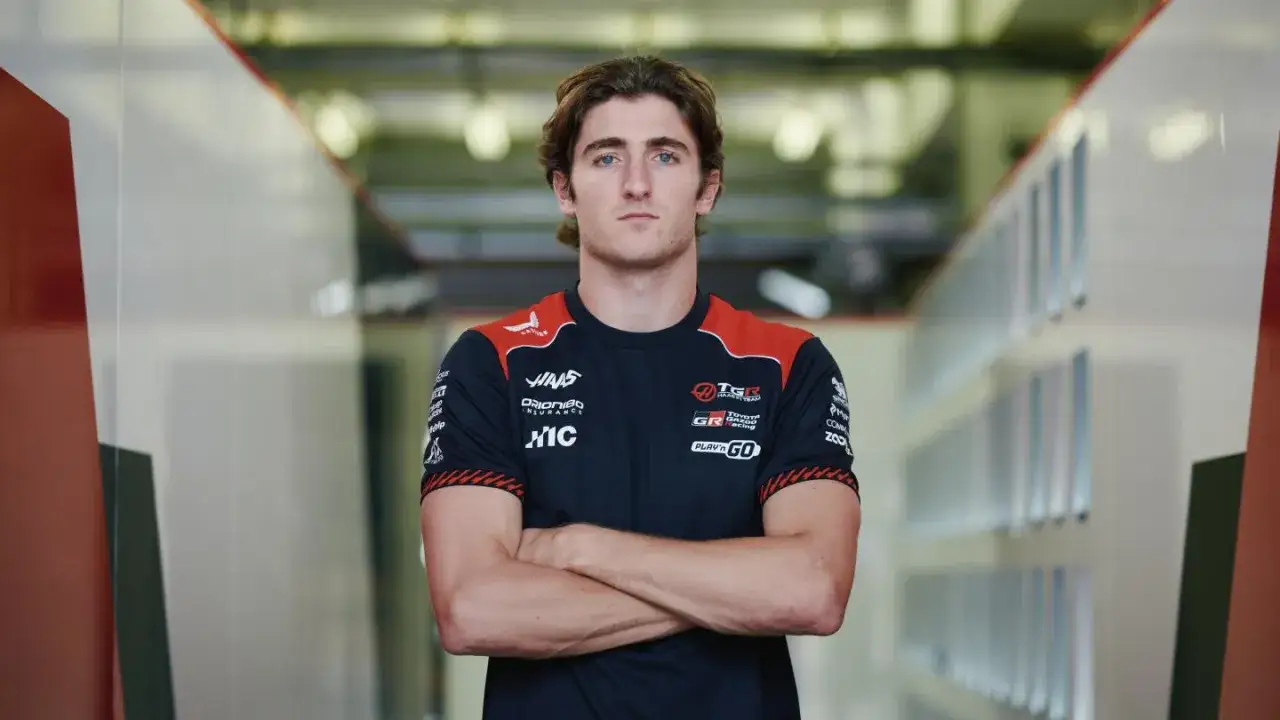 Jack Doohan, piloto de carreras, posa con los brazos cruzados en un garaje con taquillas.