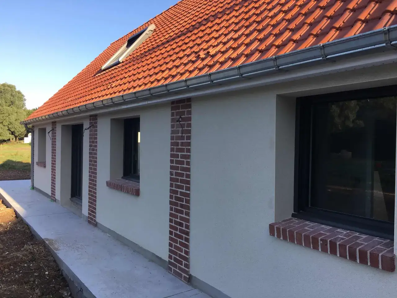 Comment cacher un vilain mur ext&eacute;rieur : des bandes de briques rouges ornent le cr&eacute;pi clair d'une maison neuve, ajoutant du cachet.