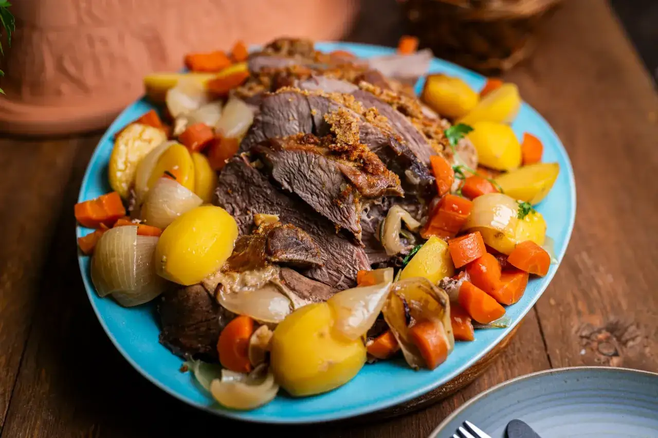 Saftiger Lammbraten nach Omas Rezept, serviert mit Kartoffeln, Karotten und Zwiebeln auf einem blauen Teller.