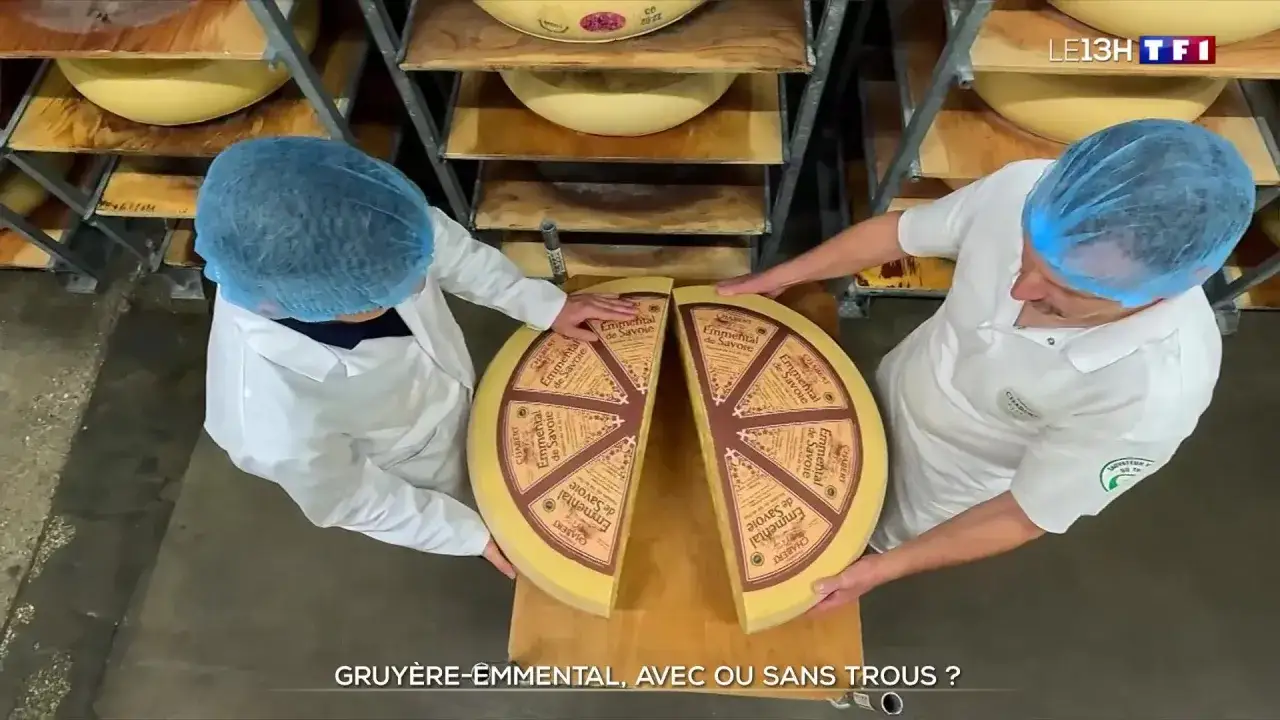 Deux fromagers pr&eacute;sentent un grand fromage coup&eacute; en deux, illustrant la diff&eacute;rence entre gruy&egrave;re et emmental.