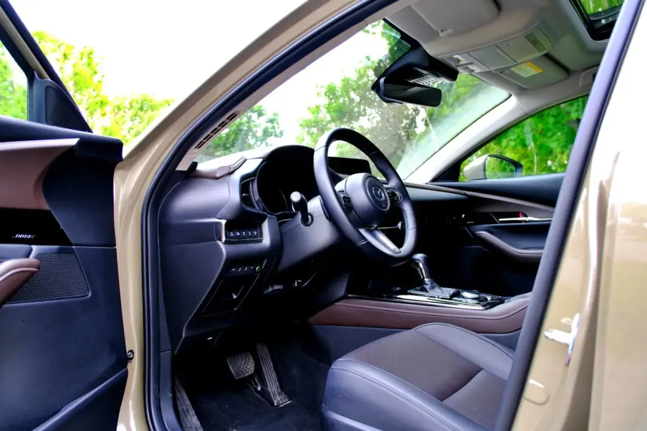 Wnętrze Mazdy CX-30 z widokiem na deskę rozdzielczą, kierownicę i fotel. Eleganckie detale i komfortowe siedzenia zapraszają do podróży.