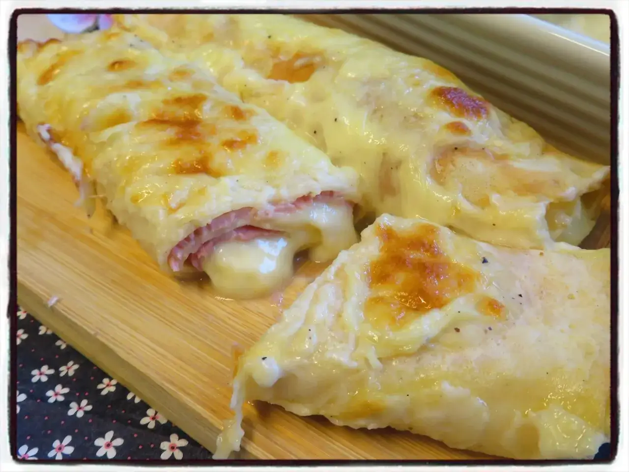 Trois cr&ecirc;pes au jambon et fromage fondant, gratin&eacute;es et dor&eacute;es, servies sur une planche en bois.
