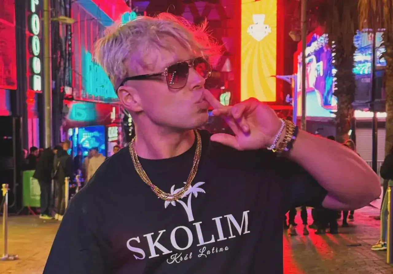 Skolim, Król Latino, w czarnej koszulce z palmami, pozuje na tle neonów. Ile lat ma Skolim?