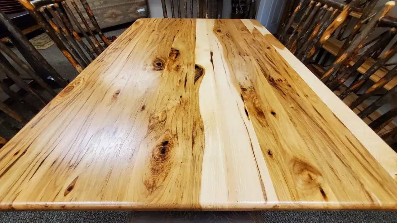 A rustic wood table with a natural, unfinished look, showcasing unique grain patterns and knots. The chairs are made of branches, complementing the table's organic style.