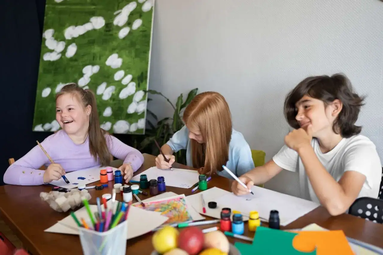 Three children enjoy art programs, painting and drawing at a table filled with colorful supplies.