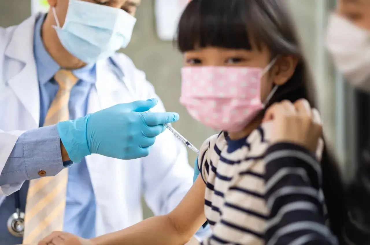 Lekarz w masce podaje szczepionkę HPV dziecku. Niektórzy obawiają się, że szczepionka HPV jest szkodliwa.