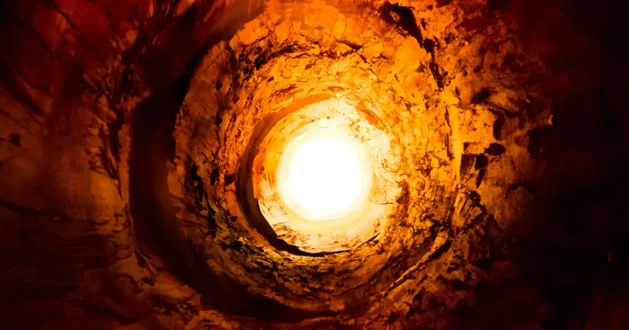 Wnętrze skalnego tunelu, oświetlone jasnym światłem u wylotu, przypomina najgłębszy odwiert.