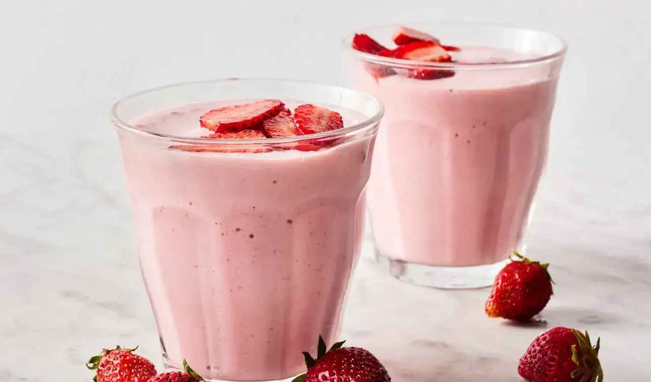 Dos vasos de batido de fresa y plátano, decorados con rodajas de fresa fresca.