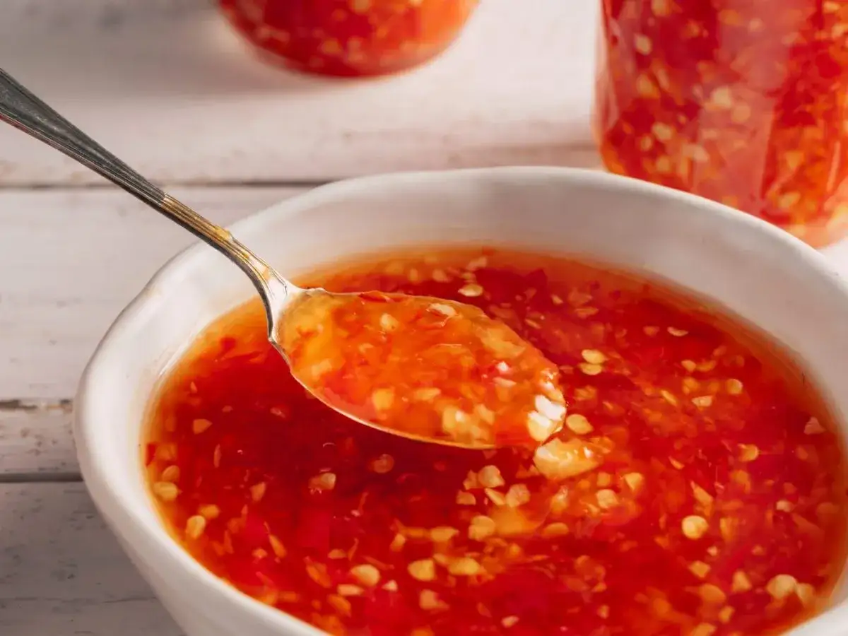 Ein Löffel voller leuchtend roter Sweet Chilli Sauce, perfekt für Ihr nächstes Rezept. Kleine Chilistückchen und Knoblauch sind sichtbar.