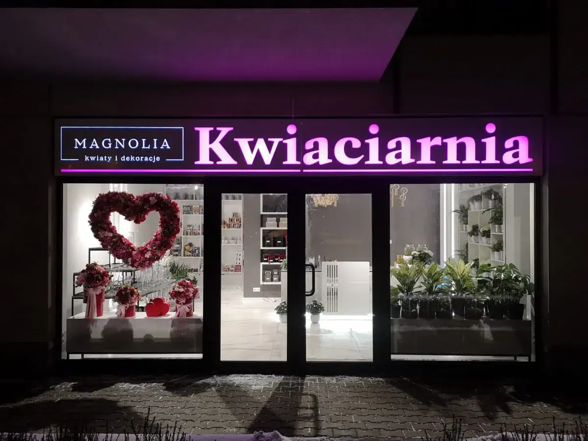 Magnolia Kwiaty i Dekoracje – urocza reklama kwiaciarni z sercem z kwiatów i roślinami w witrynie.