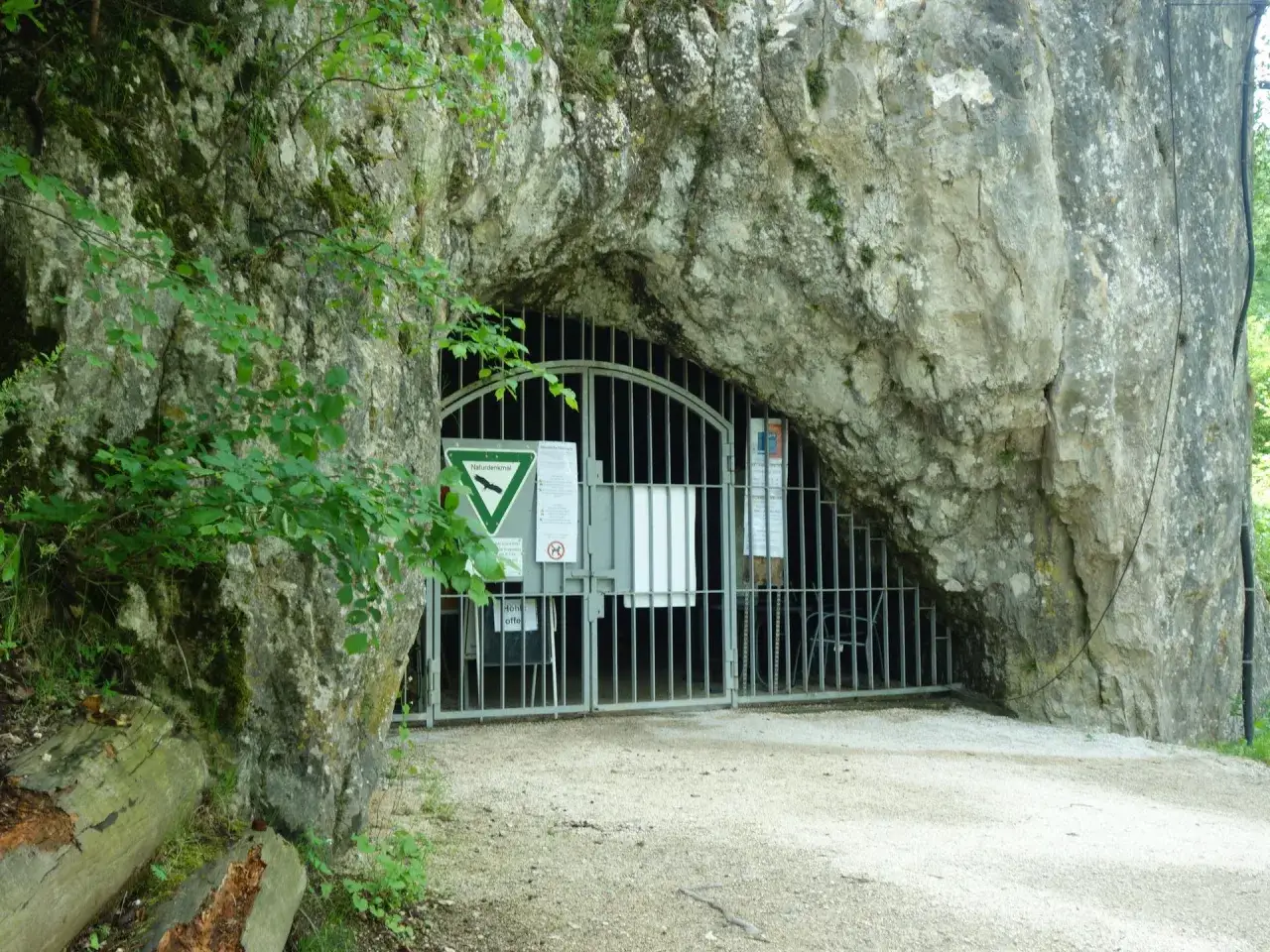 Eingang zu einer Höhle mit Gittertor, Hinweisschildern und dem Hinweis