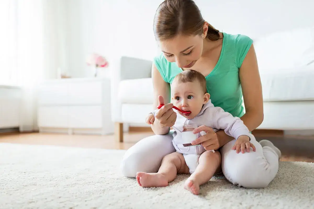 Mama karmi łyżeczką 3-miesięczne dziecko, które zaczyna poznawać nowe smaki.