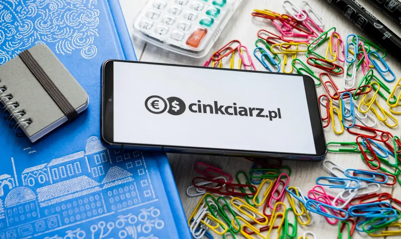 Na ekranie telefonu widnieje logo z symbolami euro i dolara oraz napis 
