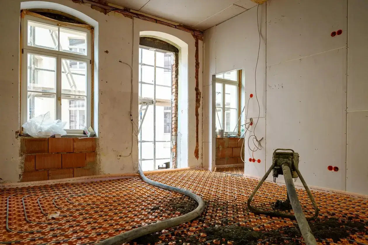 Installation d'un chauffage au sol ancienne génération, avec tuyaux orange et une machine de projection.