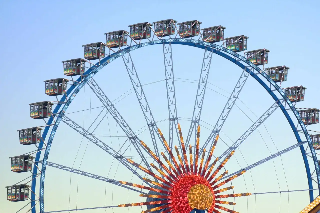 Koła widokowe z kolorowymi wagonikami na tle błękitnego nieba, przypominające atmosferę Oktoberfestu w Monachium.