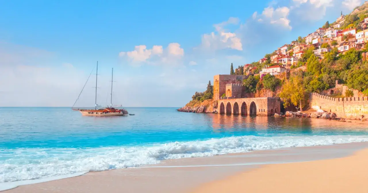 Piękna pogoda w Turcji, Alanya. Żaglówka na turkusowym morzu, zamek na wzgórzu i piaszczysta plaża.