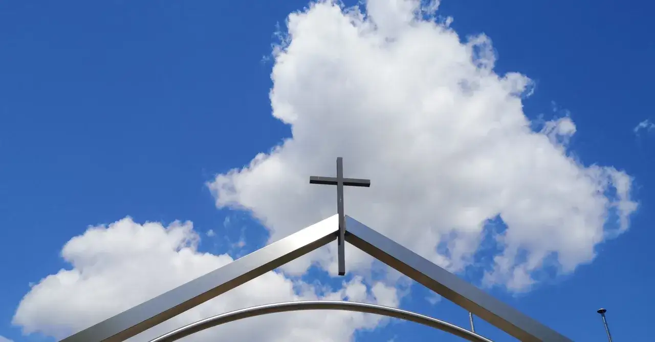 Ein Kreuz ragt in den blauen Himmel mit Wolken. Es ist ein starkes Christi Himmelfahrt Symbol.