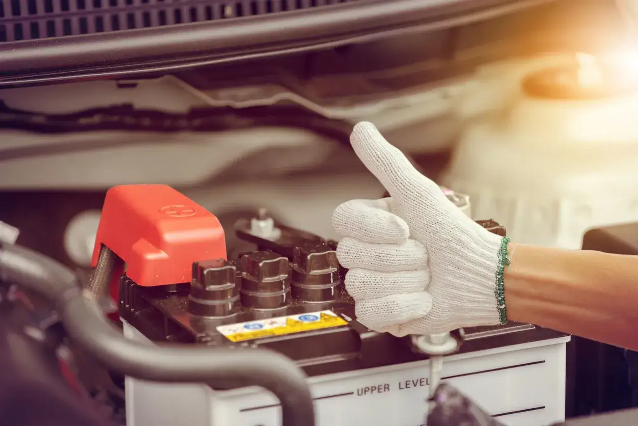 Main d'une personne portant un gant blanc fait un pouce lev&eacute; pr&egrave;s d'une batterie de voiture. Une astuce pour d&eacute;marrage &agrave; froid diesel r&eacute;ussie.