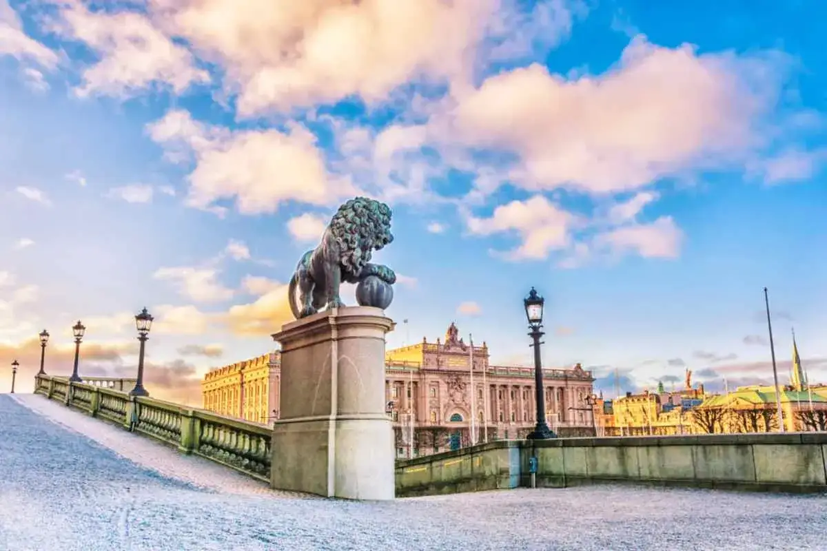 Lejonstaty vid Riksdagshuset, en del av hovet Stockholm, med en snöig bro och vackra moln på himlen.