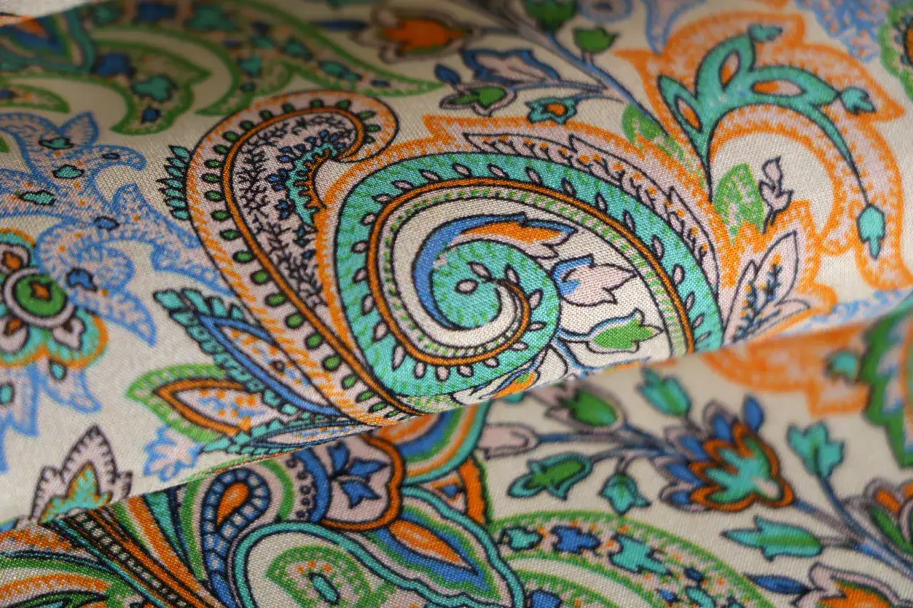 Tessuto con un motivo cachemire dai colori vivaci: arancione, turchese e blu. È la pura espressione di cos'è la fantasia, un vortice di creatività.