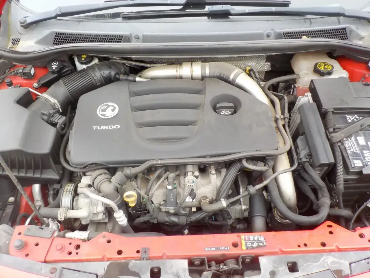 Silnik turbo z Opla Astry J po lifcie. Widoczny intercooler, kolektor dolotowy i osłona silnika z logo.