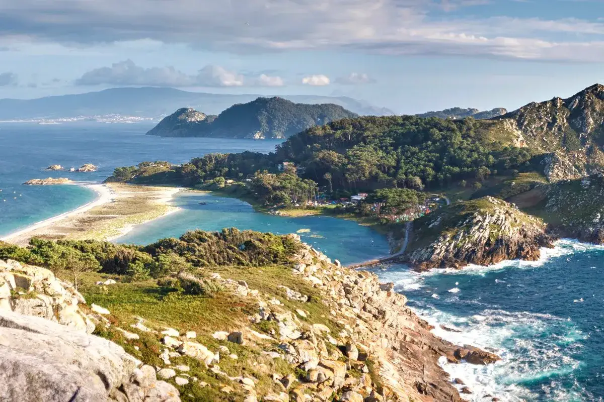 Paisaje costero con playas de arena blanca y aguas turquesas, rodeado de vegetación y rocas. Un rincón idílico de los pueblos Rías Baixas.