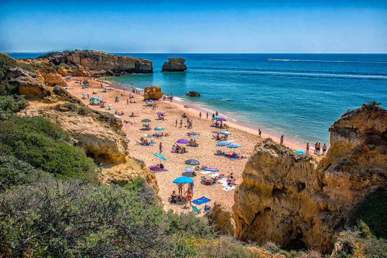 Sonniger Strand in Portugal im September. Menschen entspannen sich unter bunten Sonnenschirmen.