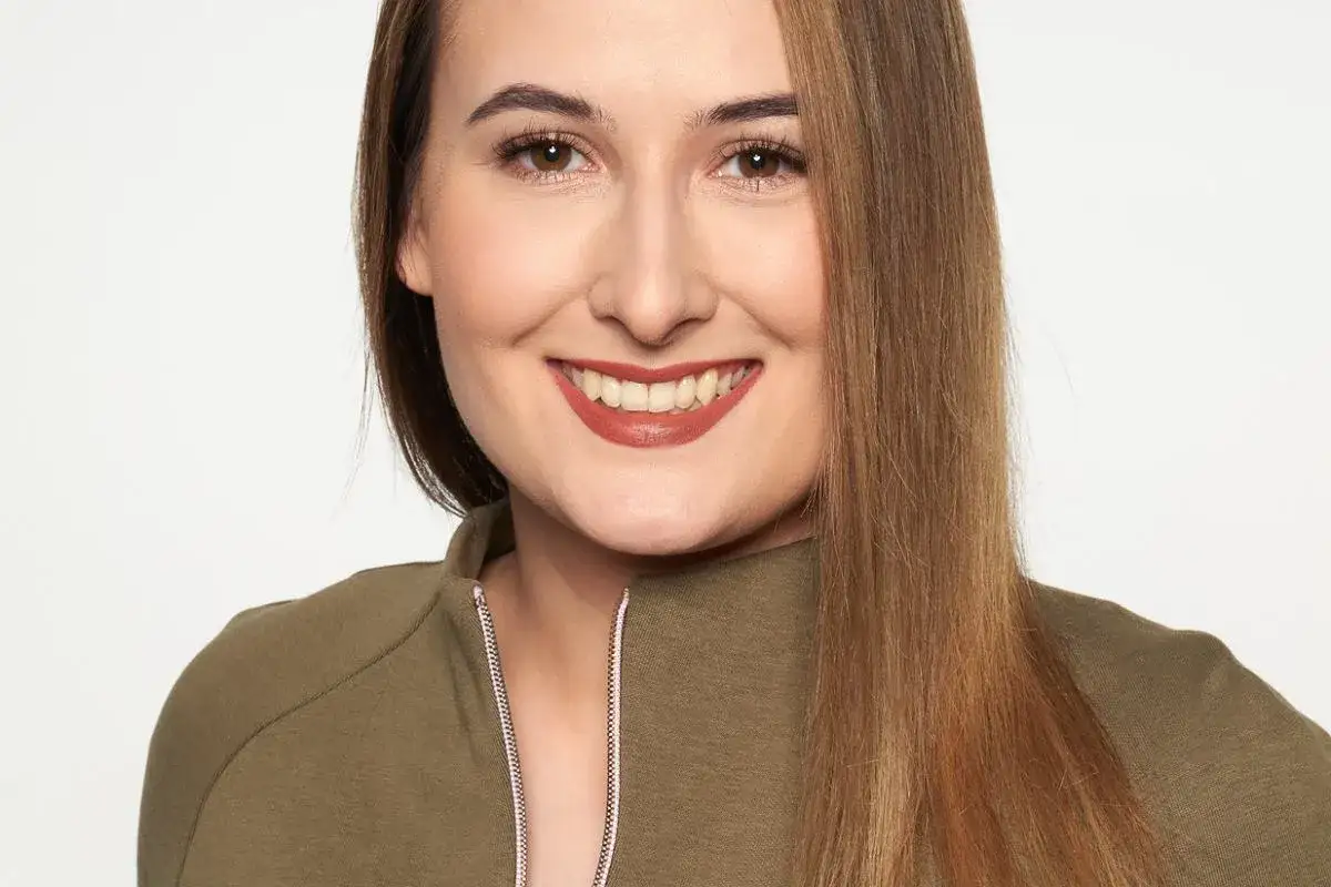 Uśmiechnięta kobieta w zielonej bluzie, z długimi, brązowymi włosami. Wygląda jak profesjonalny headhunter szukający najlepszych talentów.