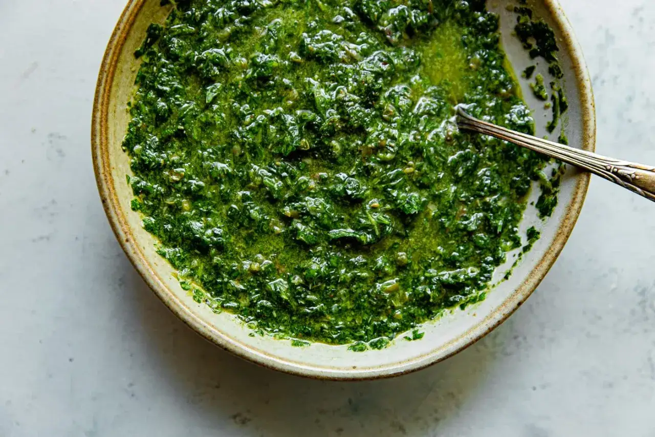 Un cuenco de cerámica con una vibrante salsa verde, con trozos de hierbas frescas y un brillo aceitoso.